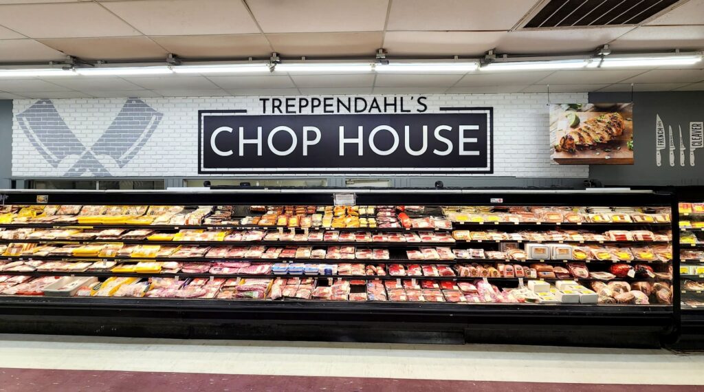 A grocery store display case of packaged meats sits beneath a 