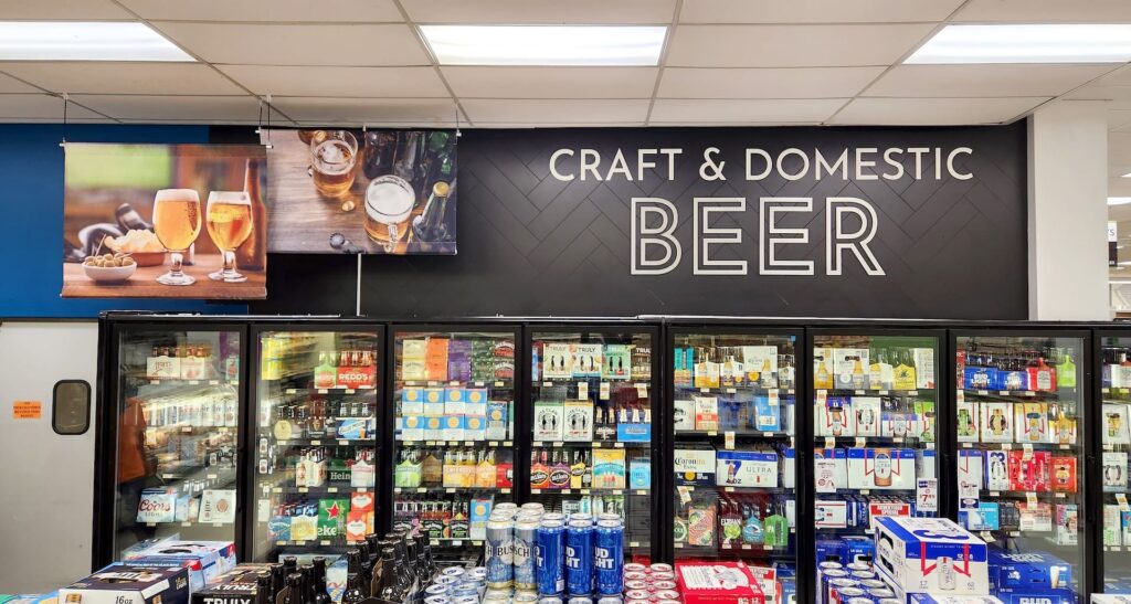 Chilled display of assorted beer cans and bottles beneath a 