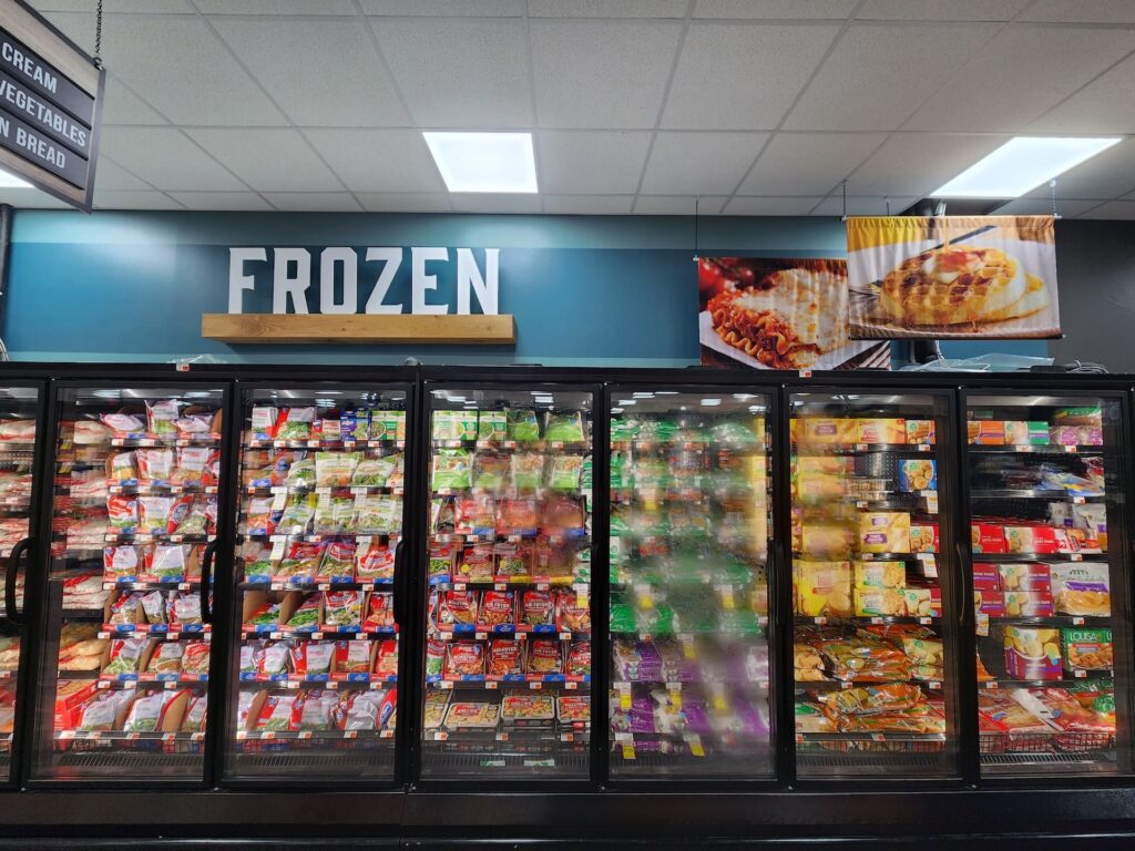 A modern grocery store freezer area filled with assorted packaged frozen foods beneath a sign that says 