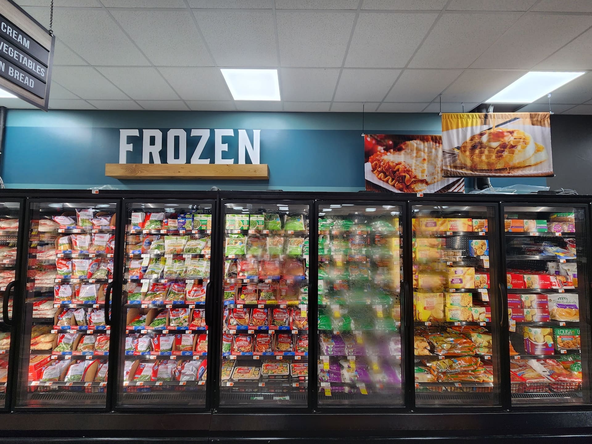 A modern grocery store freezer area filled with assorted packaged frozen foods beneath a sign that says "FROZEN.