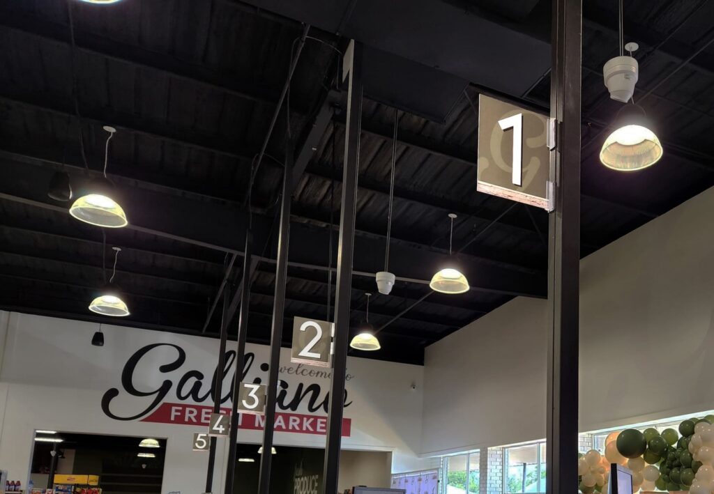 A supermarket checkout with numbered aisle signs hangs from the ceiling, blending into the store’s modern décor.