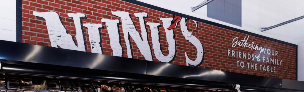 A brick wall sign displays “Nino’s” and the phrase “Gathering Your Friends & Family To The Table” on the right, creating a cozy vibe.