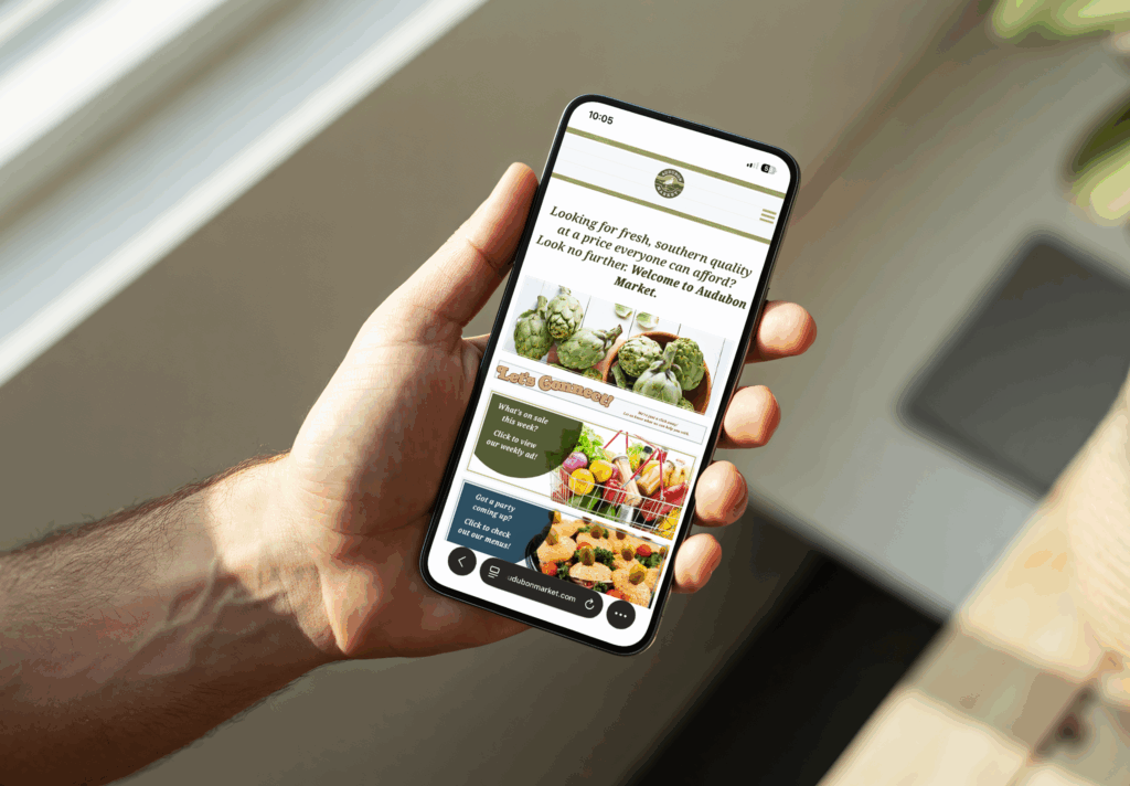 A hand holds a smartphone displaying a Digital Marketing website focused on artichokes, local produce, and fresh vegetable images.
