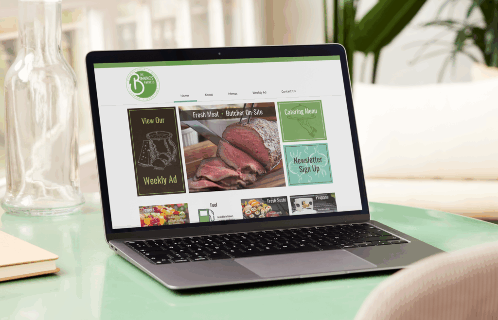 A laptop on a green table displays a butcher shop website with fresh meat ads, a catering menu, and digital marketing features.