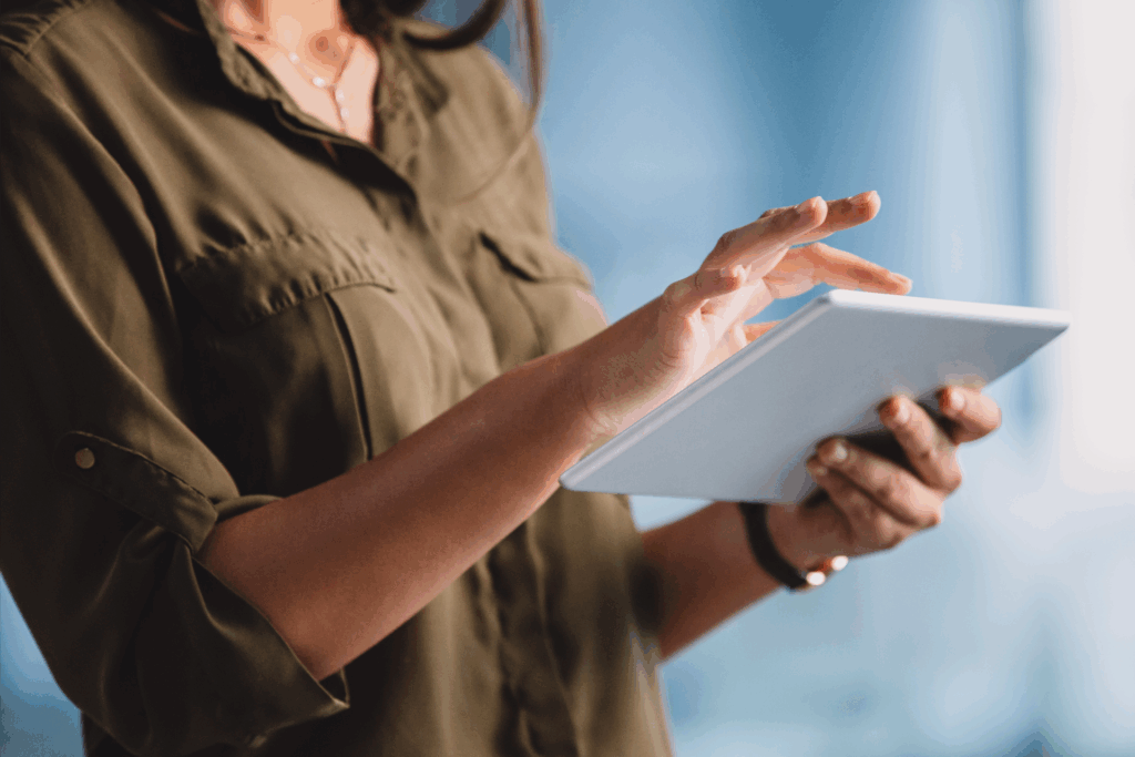 Person in an olive green shirt using a tablet, focused on digital marketing tools, against a blurred blue background.