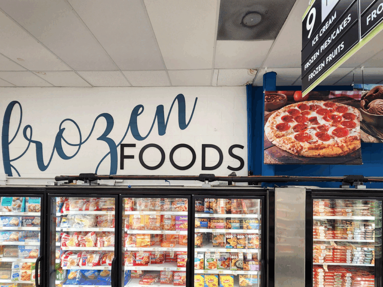Frozen foods section in a grocery store showcases Retail Decor with freezers full of products and a sign featuring pepperoni pizza.