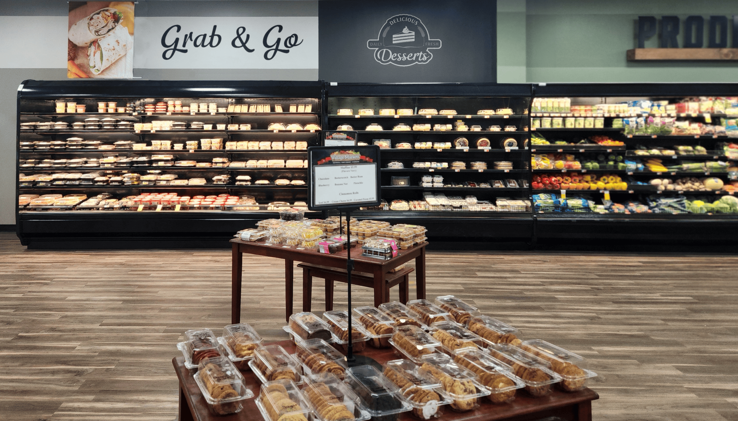 Bakery section in a grocery store with packaged desserts and pastries on display tables and shelves labeled "Grab & Go" and "Desserts".